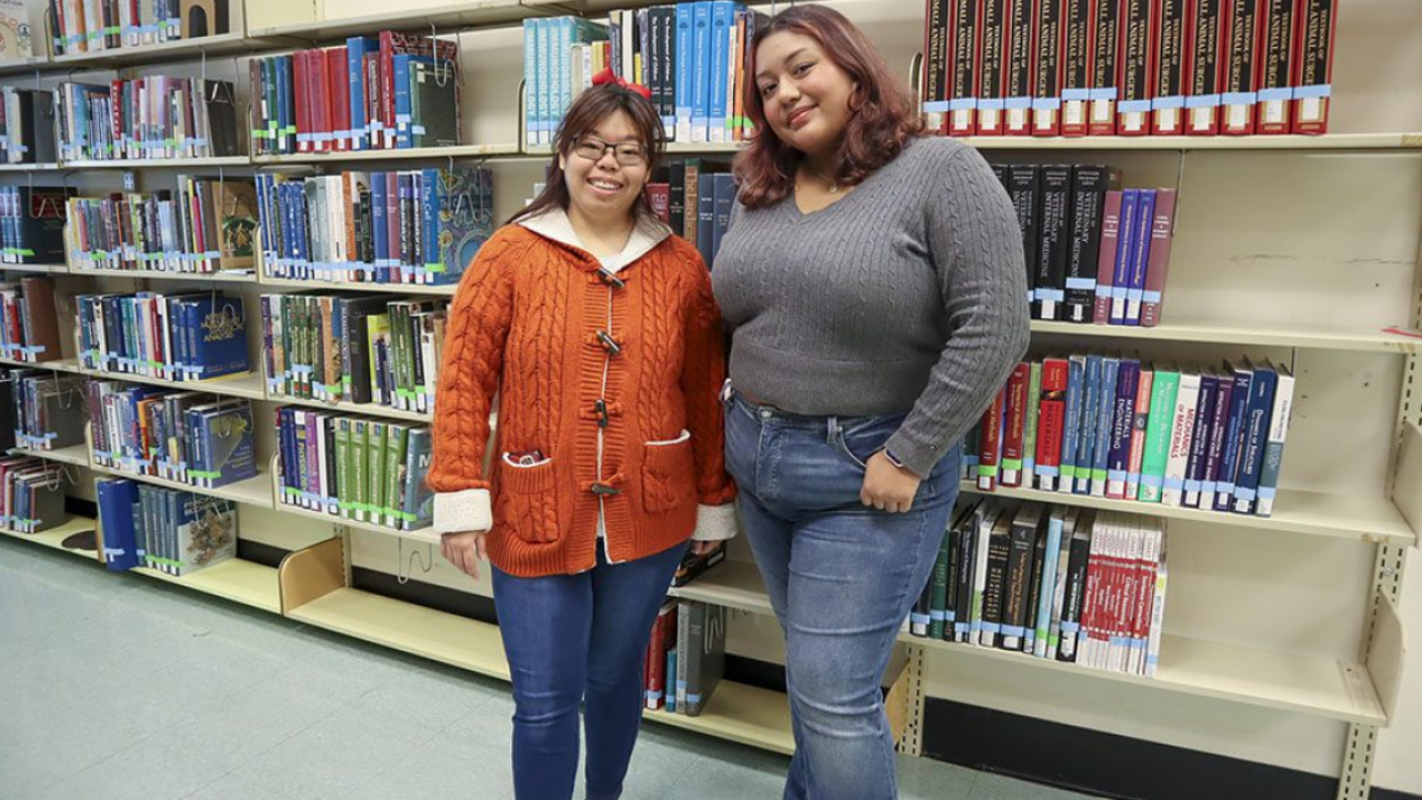 Redwood SEED Scholar Karis Chun standing with her student mentor Emily Gavidia in front of a library bookshelf