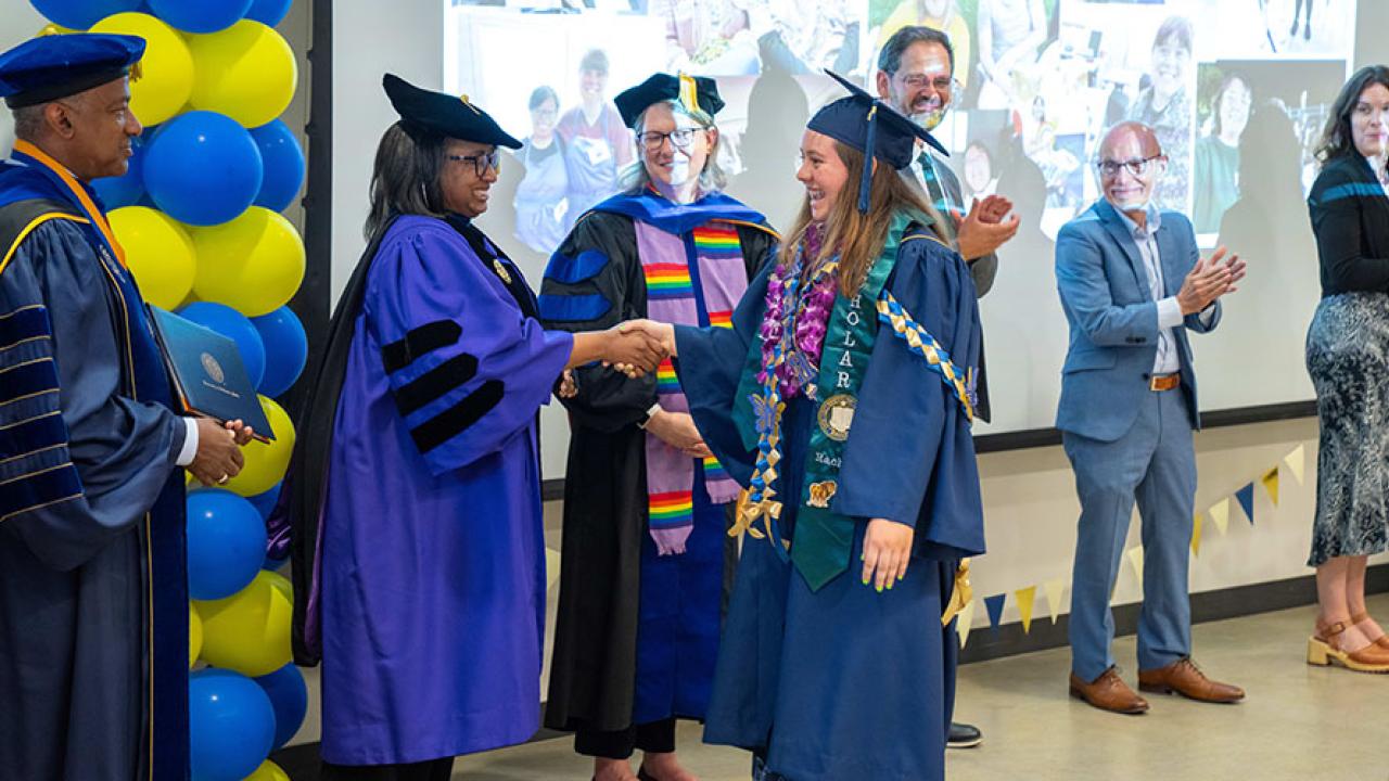 a redwood seed scholar walks across the room shaking hands with a line of people and getting a diploma