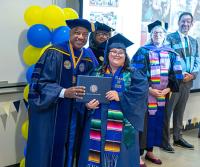 a scholar smiles with the chancellor and vice chancellor as she gets her diploma