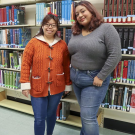 Redwood SEED Scholar Karis Chun standing with her student mentor Emily Gavidia in front of a library bookshelf